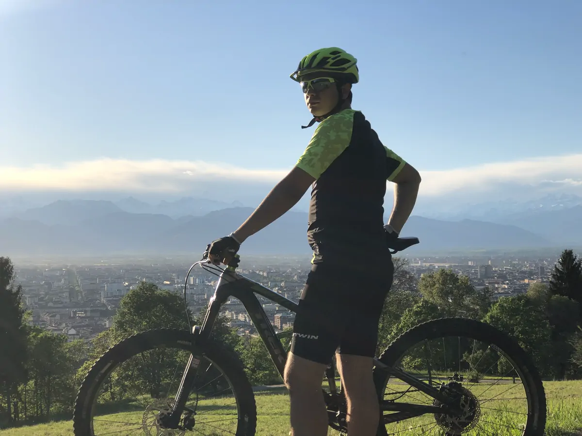 Abozar with his mountain bike on a hill above Turin, snowy mountains on the horizon