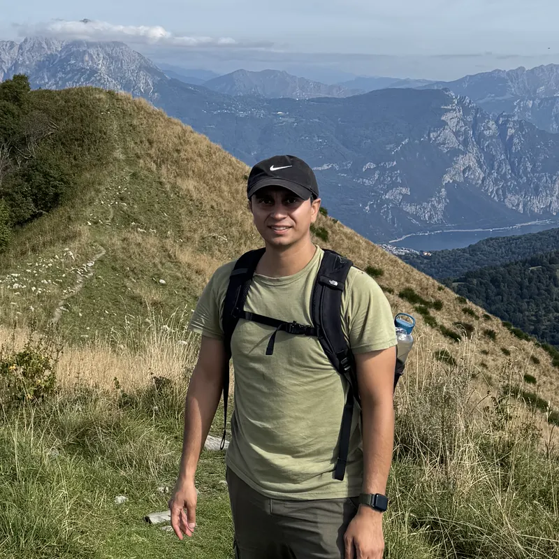 Abozar with a backpack on a grassy ridge above Lake Como