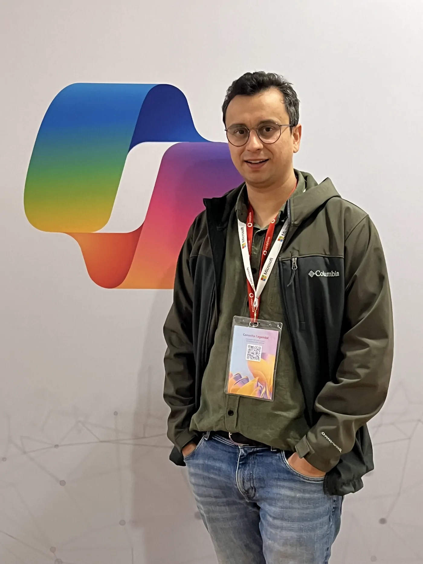 Abozar at a tech conference with a badge around his neck, a colourful Copilot logo behind him