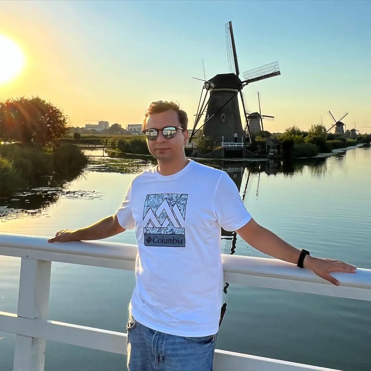Abozar on a white bridge at sunset with the Kinderdijk windmills behind him