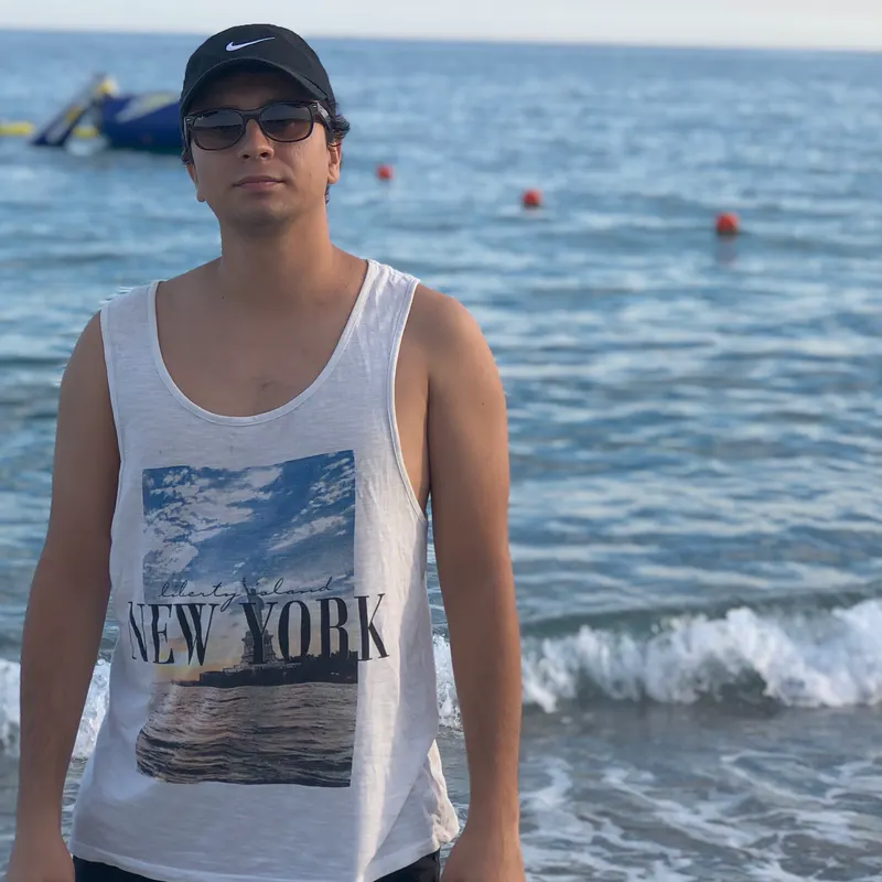 Abozar in a cap and a white tank top by the sea in Finale Ligure