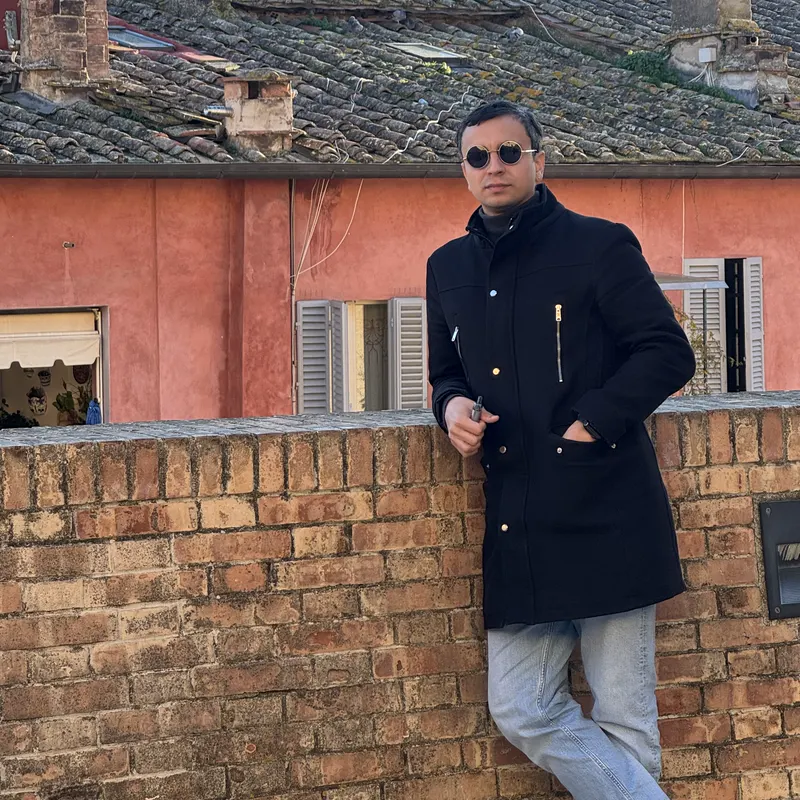 Abozar in a dark coat by a brick wall, Siena's cathedral and rooftops behind him