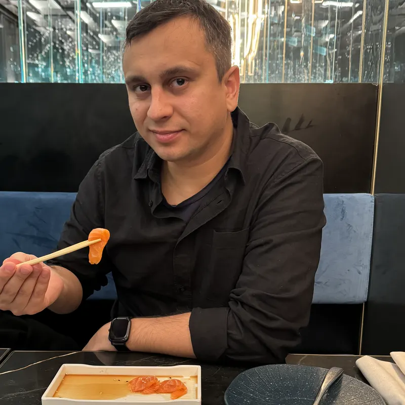 Abozar smiling at a restaurant table, holding a piece of sushi with chopsticks